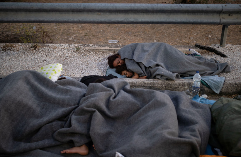 Refugees and migrants sleep on the side of a road following a fire at the Moria camp on the island of Lesbos. (photo credit: ALKIS KONSTANTINIDIS / REUTERS)