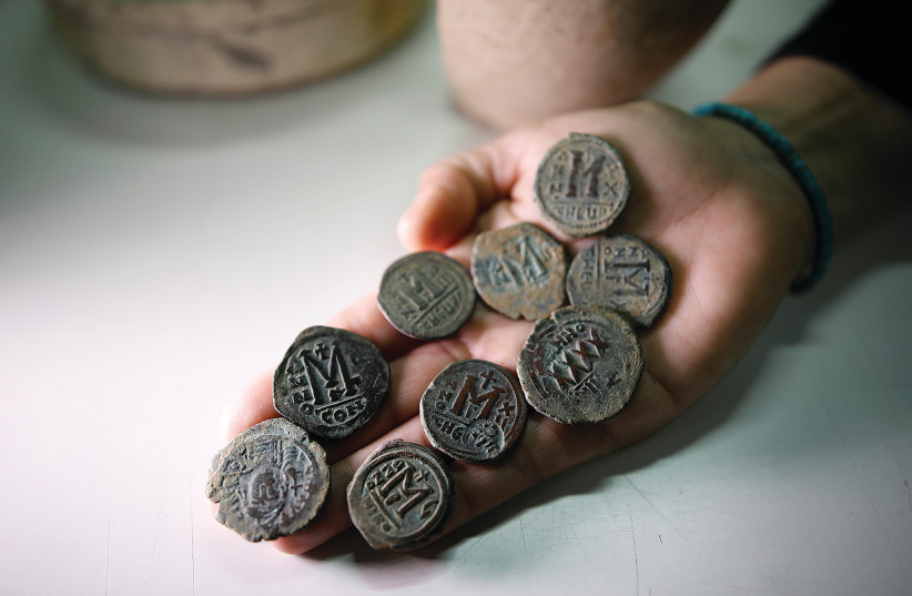 An archaeologist holds bronze coins from the Byzantine period during a media tour at Israel's National Treasures Storeroom, Beit Shemesh, March 19, 2017 (credit: REUTERS/AMIR COHEN)