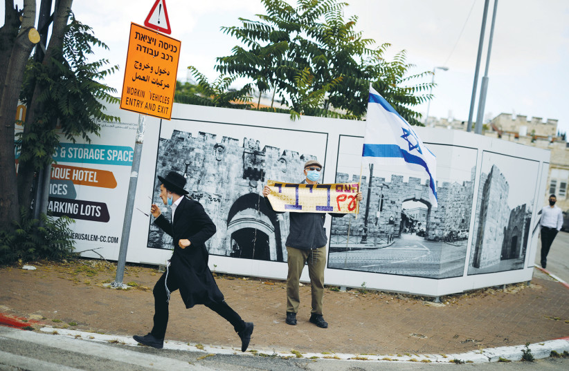 AN ULTRA-ORTHODOX man walks past a supporter of Prime Minister Benjamin Netanyahu holding a placard reading, ‘The nation is with Bibi,’ in May, 2020. (photo credit: AMIR COHEN/REUTERS)