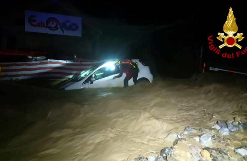A firefighter is seen next to a partially submerged car after heavy rains caused flooding in the town of Limone Piemonte, Italy, October 2, 2020. Picture taken October 2, 2020.  (photo credit: VIGILI DEL FUOCO/HANDOUT VIA REUTERS)