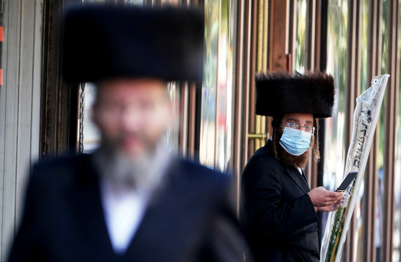 ULTRA-ORTHODOX men – one masked, one not – are seen in the haredi enclave of Borough Park in Brooklyn, New York, on October 6.  (credit: CARLO ALLEGRI/REUTERS)