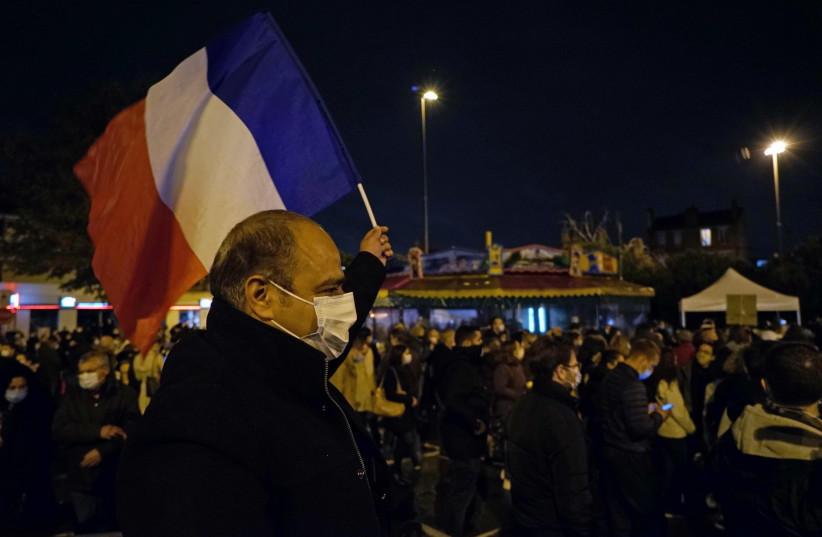 A man waves a French national flag during a silent march to pay tribute to Samuel Paty, the French teacher who was beheaded on the streets of the Paris suburb of Conflans-Sainte-Honorine, France, October 20, 2020 (photo credit: REUTERS/LUCIEN LIBERT)