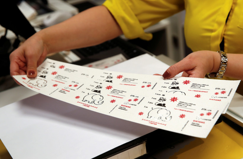 An employee of the Austrian postal service holds a sheet of so-called "corona stamps" in a post office, as the 2.75 euro "corona stamp" is printed on three-ply toilet paper and sold individually as part of a 10 cm wide sheet, in Vienna, Austria October 23, 2020.  (photo credit: REUTERS)