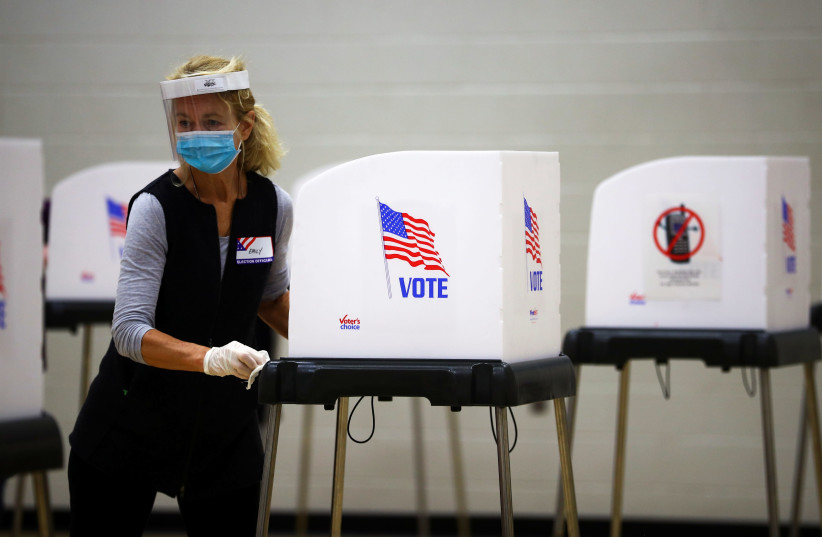 A woman cleans a voting booth at a polling station located at the McFaul Activity Center in Bel Air, Harford County, during early voting in Maryland, US, October 27, 2020 (photo credit: REUTERS / HANNAH MCKAY)