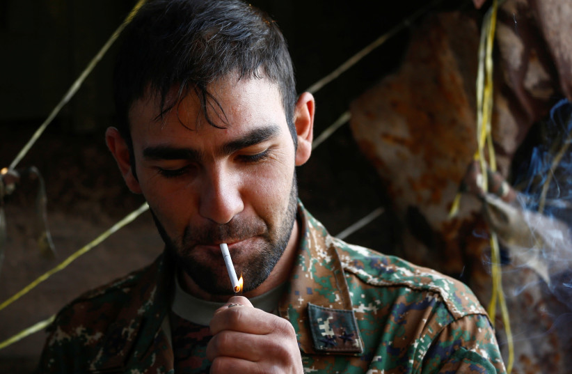 An Ethnic Armenian soldier smokes a cigarette at fighting positions on the front line during a military conflict against Azerbaijan's armed forces in the breakaway region of Nagorno-Karabakh, October 20, 2020. (photo credit: STRINGER/ REUTERS)