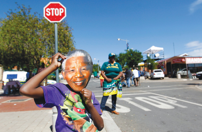 A BOY WEARS a mask of the late South African president Nelson Mandela outside his former house in Soweto. (photo credit: THOMAS MUKOYA / REUTERS)