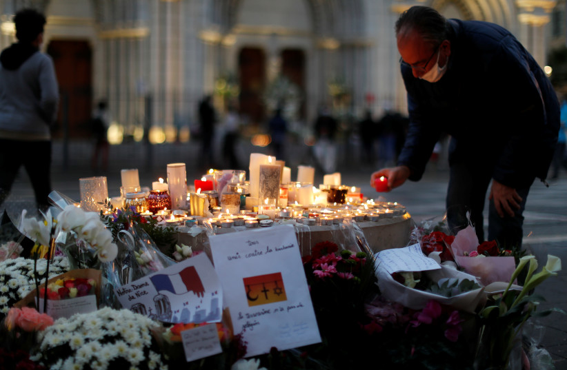 A man lights a candle near the Notre Dame church in tribute to the victims of a deadly knife attack in Nice, France, October 30, 2020 (photo credit: REUTERS/ERIC GAILLARD)
