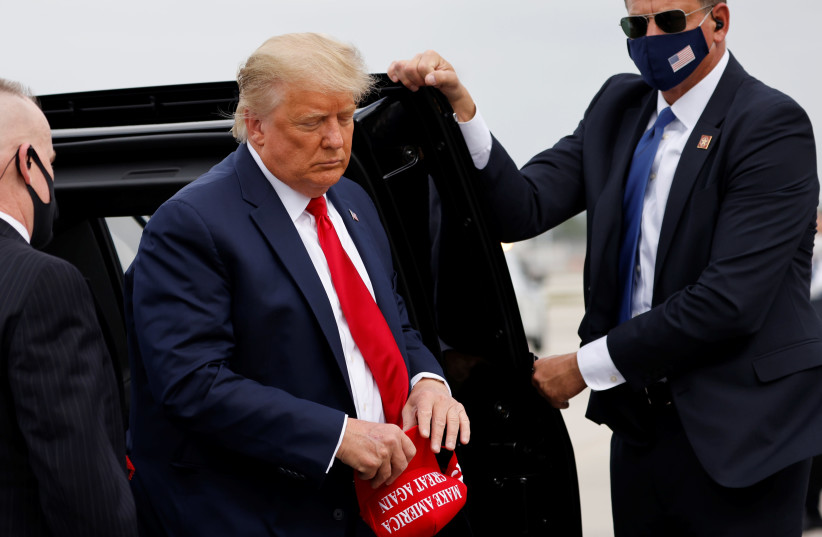 U.S. President Donald Trump holds a 'Make America Great Again' cap while arriving to board Air Force One as he departs Florida for campaign travel to North Carolina, Pennsylvania, Michigan and Wisconsin at Miami International Airport in Miami, Florida, U.S., November 2, 2020 (photo credit: CARLOS BARRIA / REUTERS)