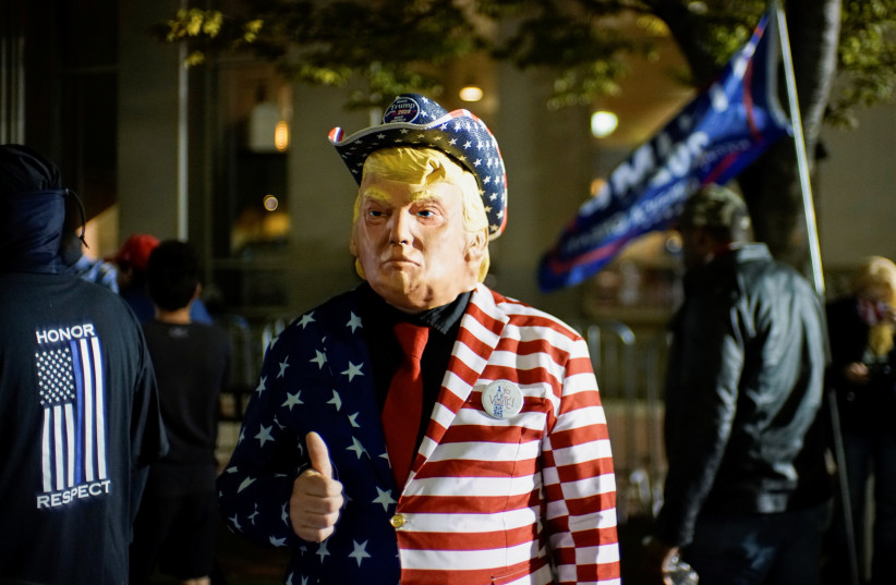 A supporter of US President Donald Trump dressed with the US flag colors and a mask depicting Trump gives a thumbs up as votes continue to be counted. November 6, 2020 (photo credit: EDUARDO MUNOZ / REUTERS)