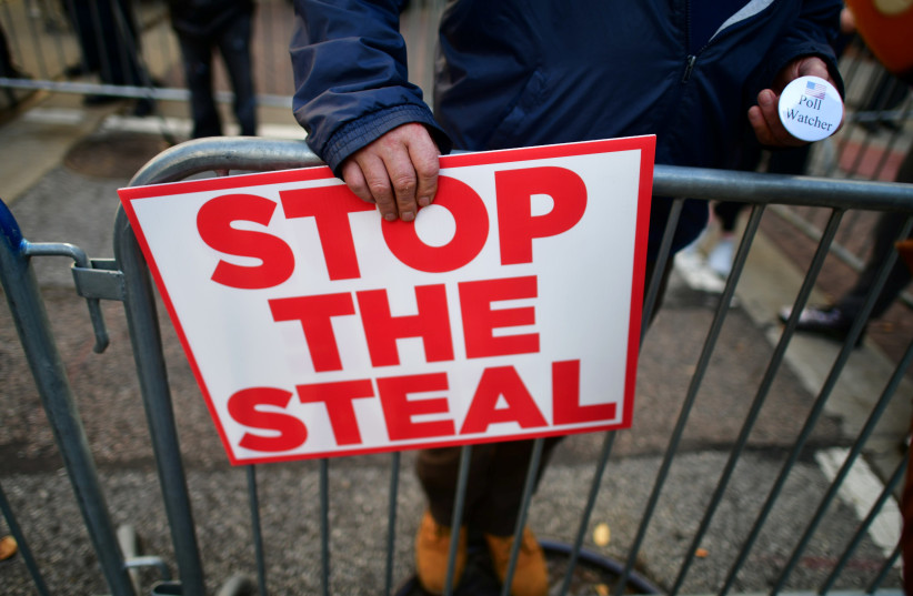 A supporter of President Donald Trump holds a sign stating "STOP THE STEAL" and a pin stating "Poll Watcher" after Democratic presidential nominee Joe Biden overtook President Donald Trump in the Pennsylvania general election vote count across the street from where ballots are being counted, three d (photo credit: REUTERS)