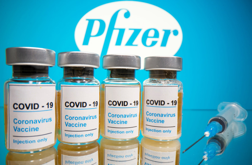 Vials with a sticker reading, "COVID-19 / Coronavirus vaccine / Injection only" and a medical syringe are seen in front of a displayed Pfizer logo in this illustration taken October 31, 2020 (photo credit: REUTERS/DADO RUVIC/ILLUSTRATION/FILE PHOTO)