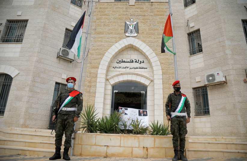 Security forces beside Palestinian flags at half-mast after Abbas declared a three-day mourning period for Saeb Erekat (photo credit: REUTERS/RANEEN SAWAFTA)