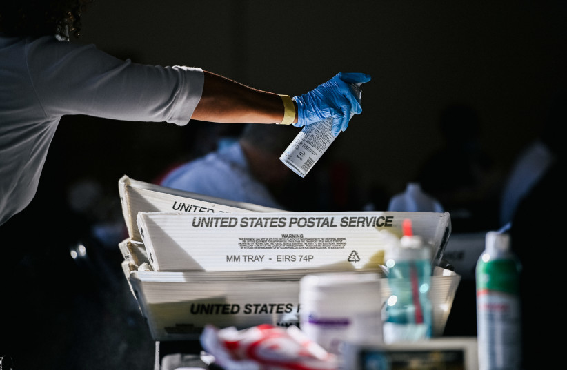 An employee of the Fulton County Board of Registration and Elections disinfects plastic trays while processing ballots in Atlanta, Georgia, US, November 4, 2020.  (photo credit: REUTERS/BRANDON BELL)
