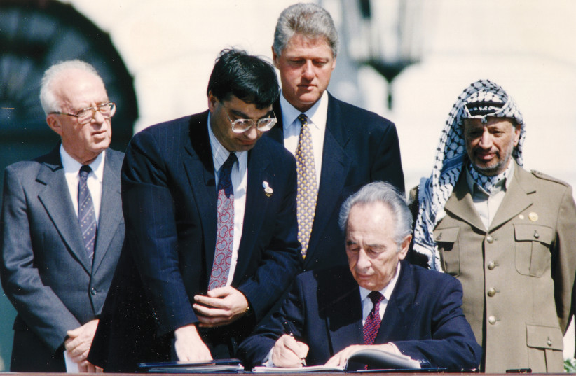FOREIGN MINISTER Shimon Peres signs the Israel-PLO peace accord, watched by PLO chairman Yasser Arafat, prime minister Yitzhak Rabin and US president Bill Clinton, at the White House in Washington, DC, September 13, 1993. (photo credit: GARY HERSHORN/REUTERS)