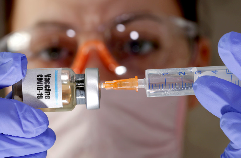 A woman holds a small bottle labeled with a "Vaccine COVID-19" sticker and a medical syringe in this illustration taken April 10, 2020. (photo credit: REUTERS)