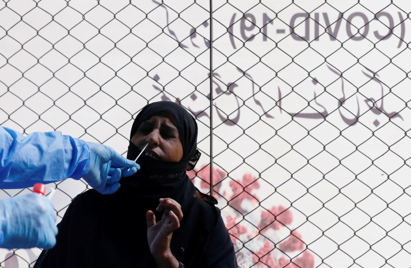 A healthcare worker takes a swab sample from a woman to be tested for the coronavirus disease (COVID-19) in Karachi, Pakistan (photo credit: AKHTAR SOOMRO / REUTERS)