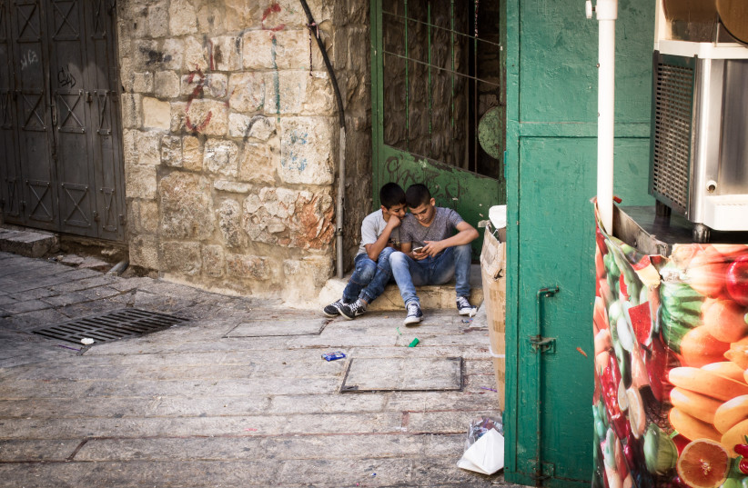 Two arab boys sit on the Street with their phone seen near Via Dolorosa in Jerusalem's Old City on October 5th, 2016. (photo credit: PHOTO BY SEBI BERENS/FLASH 90)