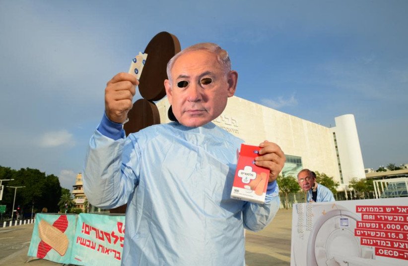 Activist from the Social Justice Centers with a facemask of Prime Minister Benjamin Netanyahu hands out a Band-Aid to protest the quick fix of the government's policies, Tel Aviv, December 2, 2020 (photo credit: AVSHALOM SASSONI/ MAARIV)