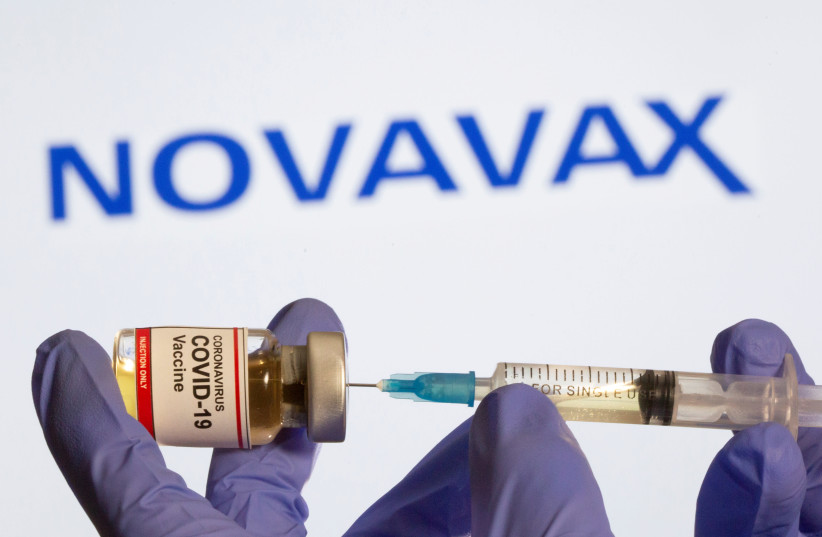 A woman holds a small bottle labeled with a "Coronavirus COVID-19 Vaccine" sticker and a medical syringe in front of displayed Novavax logo in this illustration taken, October 30, 2020. (photo credit: REUTERS/DADO RUVIC)
