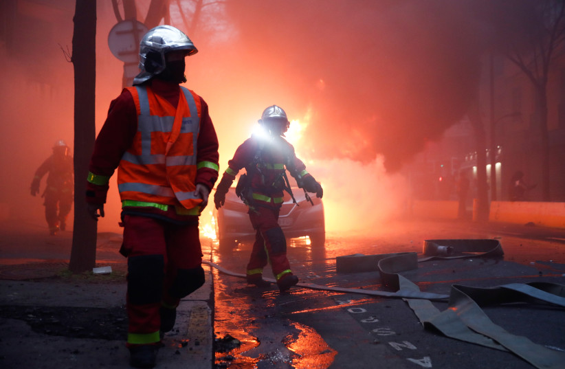 A firefighter uses a flashlight amid smoke next to burning vehicles during a protest against the "Global Security Bill'', that right groups say would make it a crime to circulate an image of a police officer's face and would infringe journalists' freedom in the country, in Paris, France, December 5, (photo credit: REUTERS)