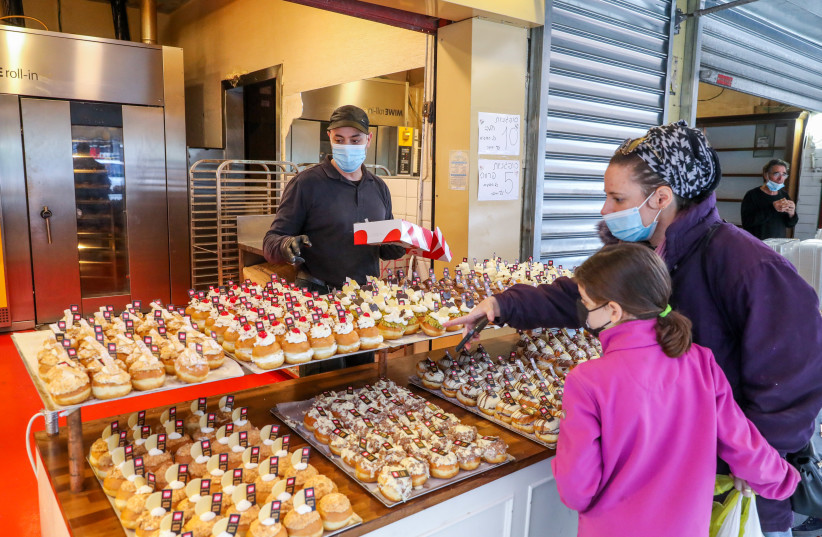Israelis are seen buying donuts ahead of Hanukkah at the Marzipan bakery near Mahane Yehuda in Jerusalem, wearing masks in accordance with coronavirus restrictions, on December 6, 2020. (credit: MARC ISRAEL SELLEM/THE JERUSALEM POST)