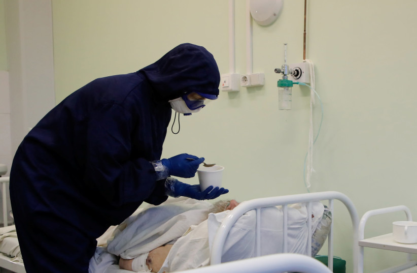 A medical specialist wearing protective gear feeds a patient at the Vologda City Hospital Number 1, where patients suffering from the coronavirus disease (COVID-19) are treated, in Vologda, Russia November 24, 2020. (photo credit: REUTERS/ANTON VAGANOV)