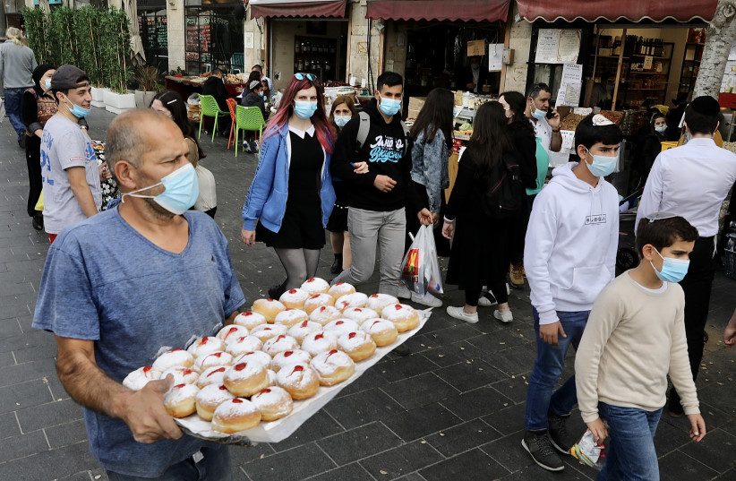 Sufganiyot, traditional treats for Hanukkah, are seen alongside Israelis walking in Jerusalem amid the coronavirus pandemic, on December 13, 2020. (photo credit: MARC ISRAEL SELLEM/THE JERUSALEM POST)