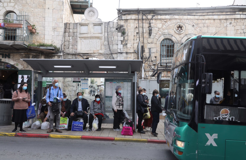 Israelis are seen waiting at a bus stop in Jerusalem amid the coronavirus pandemic, on December 13, 2020. (photo credit: MARC ISRAEL SELLEM/THE JERUSALEM POST)