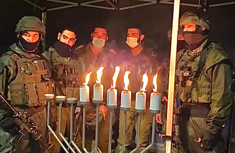 Soldiers in the IDF's Netzah Yehuda battalion are seen lighting Hanukkah candles at the Givat Assaf junction, where two of its members were murdered and a third wounded in a terrorist attack in 2018. (photo credit: NETZAH YEHUDAH)