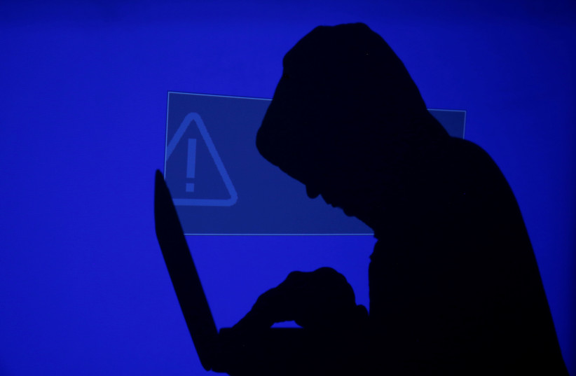 A hooded man holds a laptop computer as a blue screen with an exclamation mark is projected on him in this illustration picture taken on May 13, 2017 (photo credit: REUTERS/KACPER PEMPEL)
