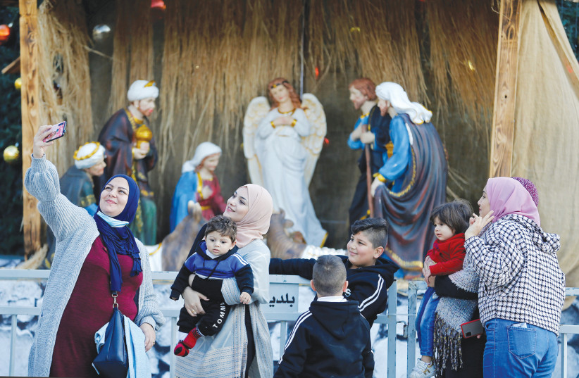 CELEBRANTS POSE for a photo in front of a nativity scene display at Manger Square ahead of Christmas in Bethlehem last week. (photo credit: MUSSA QAWASMA/REUTERS)