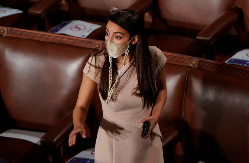 US Rep. Alexandria Ocasio-Cortez (D-NY) reacts to a colleague on the floor of the House Chamber a members of congress gathered to take their oath of office during the first session of the 117th House of Representatives on Capitol Hill in Washington, US, January 3, 2021 (photo credit: JOSHUA ROBERTS / REUTERS)
