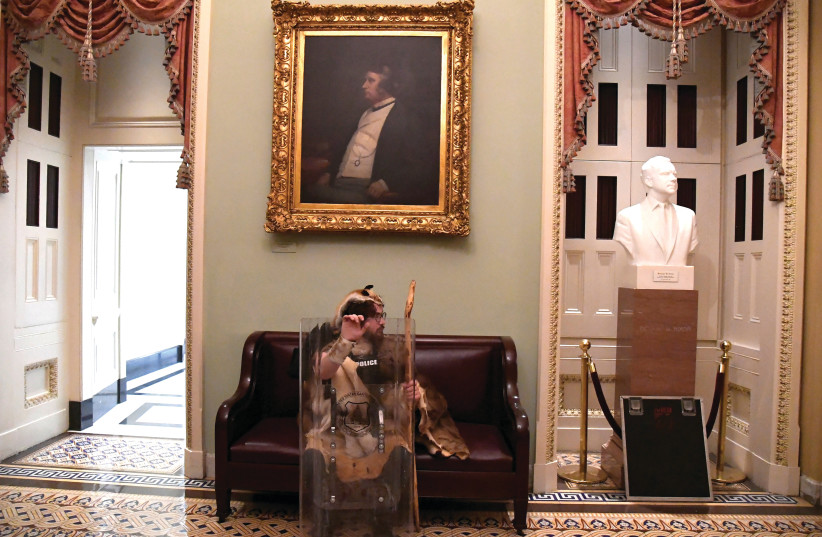 ONE OF the protesters who raided the US Captiol last week sits near the entrance to the Senate after breaching security defenses in Washington, DC. (photo credit: MIKE THEILER/REUTERS)