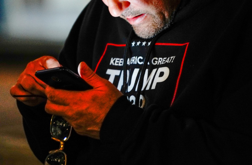 A man wearing a "Trump 2020" sweatshirt uses his mobile phone during a "Stop the Steal" protest outside Milwaukee Central Count the day after Milwaukee County finished counting absentee ballots, in Milwaukee, Wisconsin, U.S. November 5, 2020 (photo credit: BING GUAN/REUTERS)