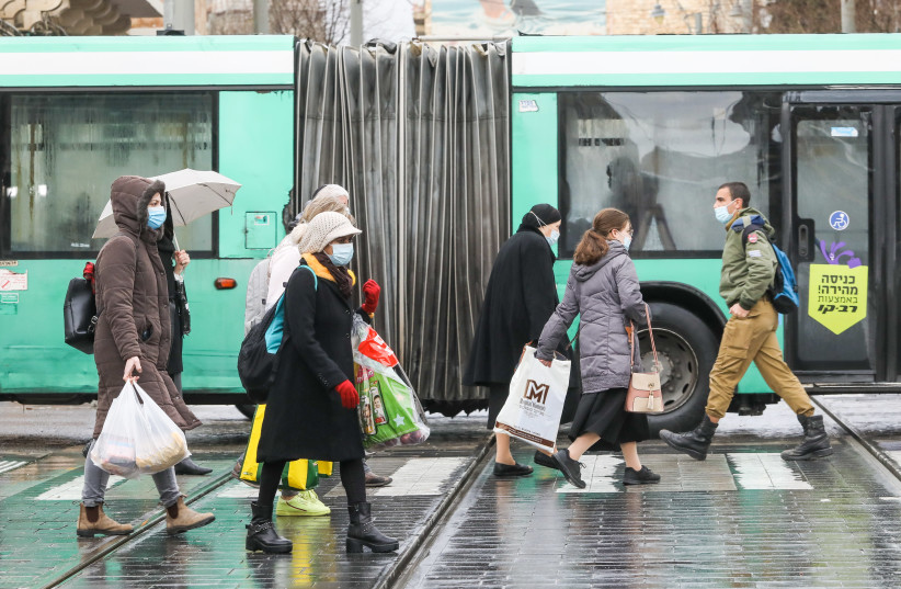 Israelis are seen walking next to a bus along the Jaffa Street light rail tracks in the rain amid the coronavirus lockdown, on January 19, 2021. (photo credit: MARC ISRAEL SELLEM/THE JERUSALEM POST)