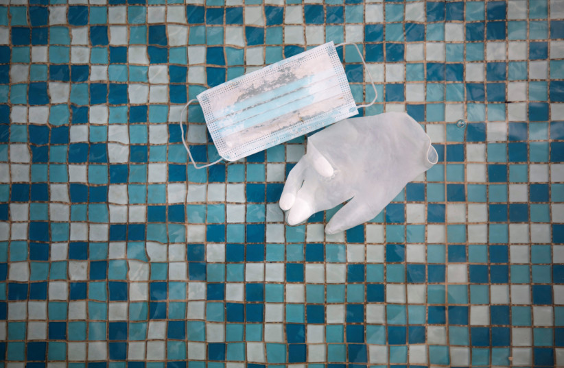 A glove and face mask float in a mosaic-covered water fountain amid Israel's third national lockdown to fight the coronavirus disease (COVID-19), in Ashkelon, Israel January 20, 2021. (photo credit: AMIR COHEN/REUTERS)
