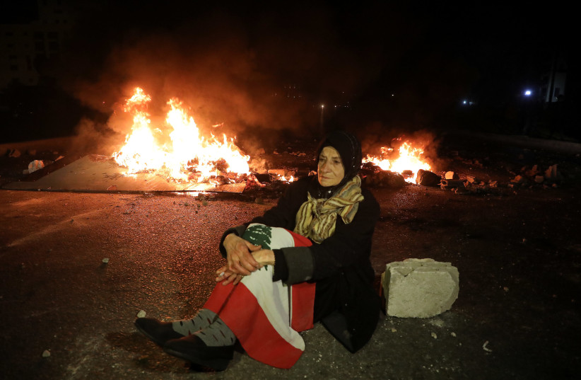 A demonstrator sits on the ground near burning fire during a protest against the fall in Lebanese pound currency and mounting economic hardship, in Beirut, Lebanon March 2, 2021. (photo credit: MOHAMED AZAKIR / REUTERS)