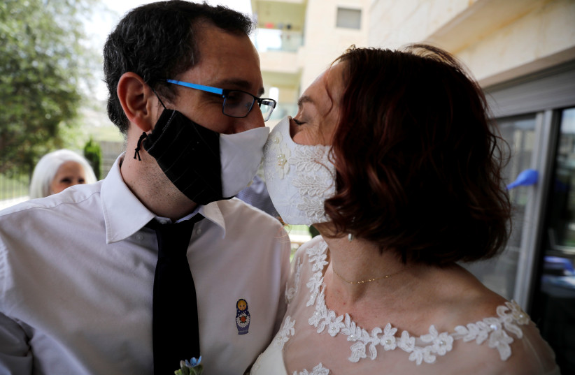 An illustrative photograph: Bride Osnat Baron and groom Yaniv Jenger kissing through their masks during their wedding party with a limited number of guests in the garden of a private house in Jerusalem on April 27, 2020 (photo credit: RONEN ZVULUN/ REURERS)