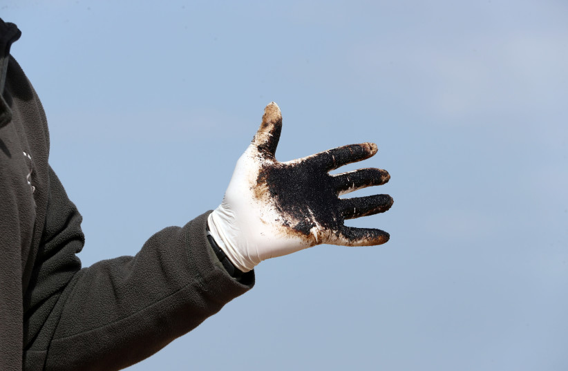 A man wears a glove covered with tar as Israeli soldiers and volunteers clean tar from the sand after an offshore oil spill drenched much of Israel's Mediterranean shoreline, at a beach in Atlit, Israel February 22, 2021.  (photo credit: REUTERS/RONEN ZEVULUN)
