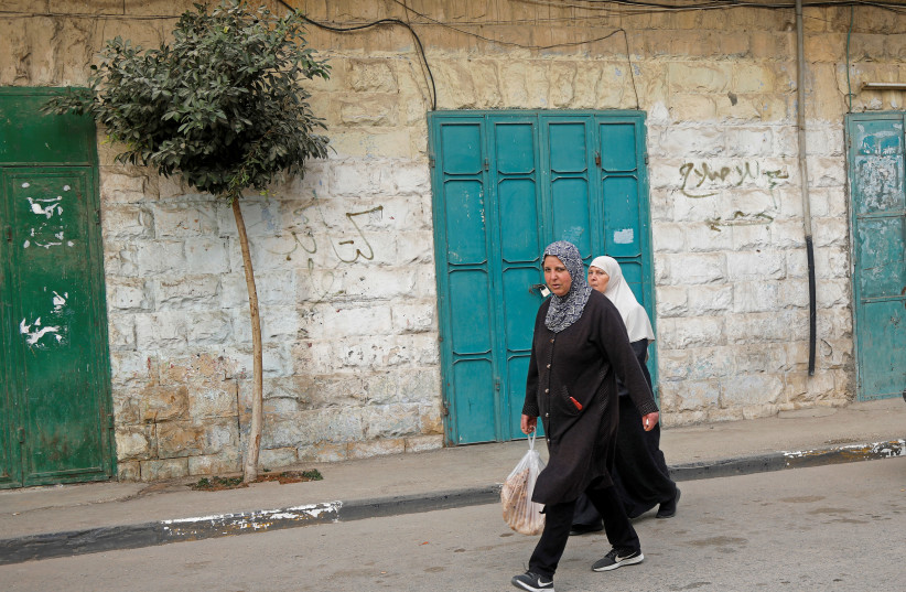 Palestinians walk past closed shops during a lockdown imposed to prevent the spread of the coronavirus disease (COVID-19), in Tubas in the West Bank March 15, 2021.  (photo credit: REUTERS/RANEEN SAWAFTA)