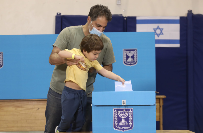 Man allows his son to cast his vote into the ballot in March 2021 elections. (credit: MARC ISRAEL SELLEM/THE JERUSALEM POST)