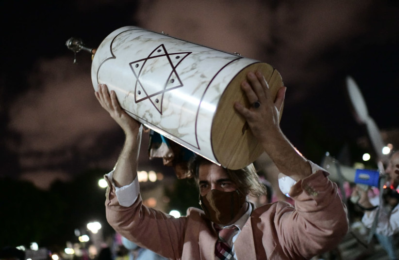 Israeli jews dance as they hold a Scroll of a Torah during Simhat Torah celebrations at Habima Square, Tel Aviv. The worshippers are marking the end of the annual cycle of the reading of the Torah and the beginning of the next cycle. October 10, 2020. Photo by Tomer Neuberg/Flash90 (credit: REUTERS/TOMER NEUBERG/FLASH90)