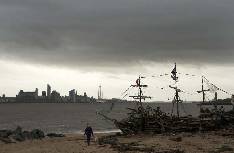 A women walks her dog under a dark sky past the Black Pearl driftwood pirate ship on New Brighton beach near Wallasey in Britain January 26, 2016. (photo credit: REUTERS)