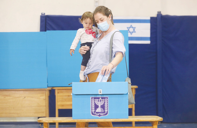 A voter holding her child casts her ballot in Jerusalem. (credit: MARC ISRAEL SELLEM)