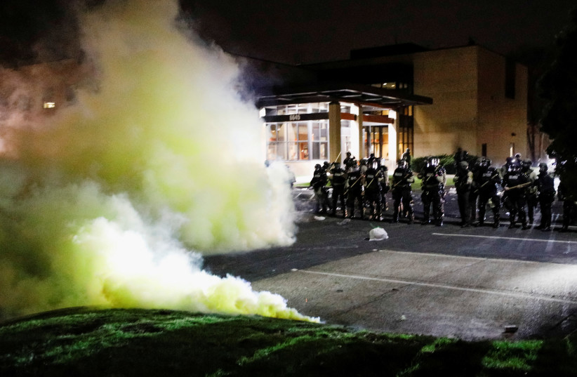Tear gas is seen as officers stand guard outside Brooklyn Center Police Department with trash thrown at them by demonstrators at their feet after police allegedly shot and killed a man, who local media report is identified by the victim's mother as Daunte Wright, in Brooklyn Center, Minnesota, US, A (photo credit: REUTERS/NICK PFOSI)