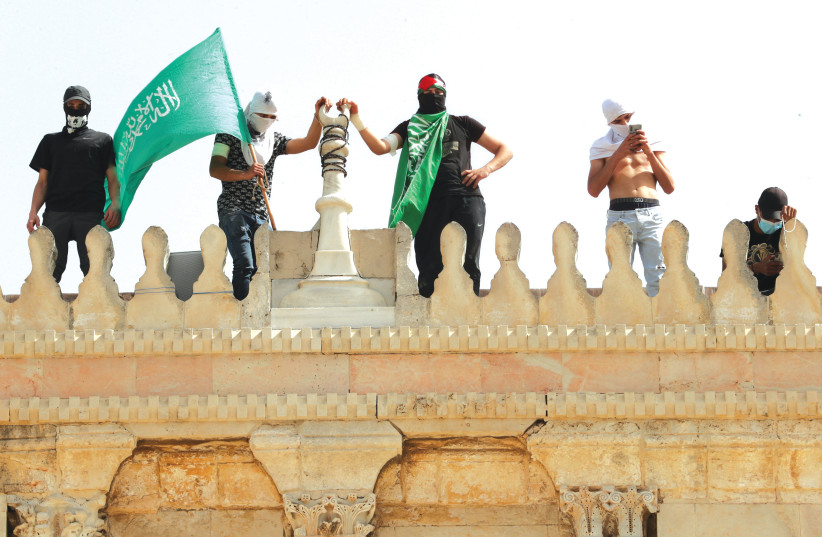 A MAN HOLDS a Hamas flag as he stands next to others atop a building near al-Aqsa Mosque in Jerusalem’s Old City on Monday. (credit: AMMAR AWAD/REUTERS)