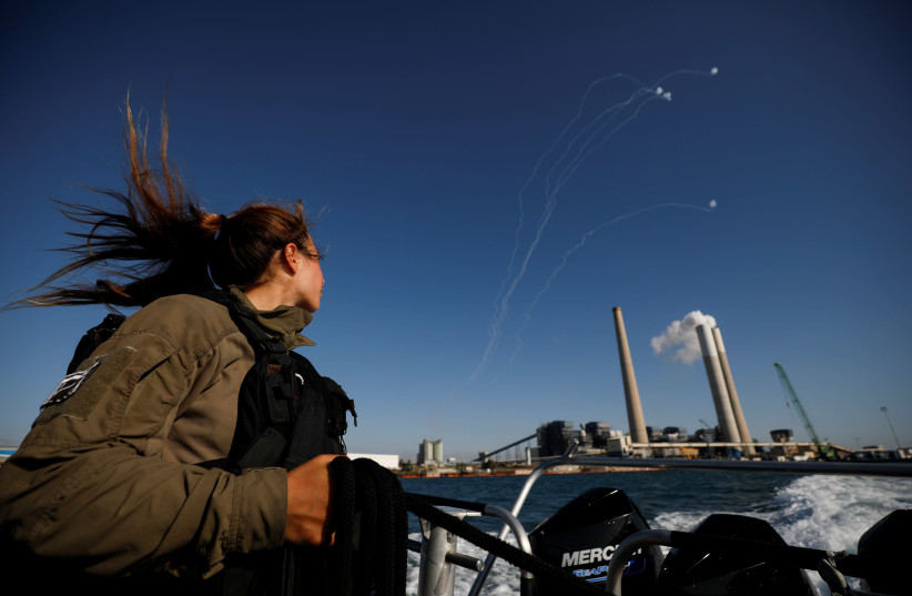 An Israeli soldier looks on as Israel's Iron Dome anti-missile system intercept rockets launched from the Gaza Strip towards Israel, as it seen from a naval boat patrolling the Mediterranean Sea off the southern Israeli coast as Israel-Gaza fighting rages on May 19, 2021. (photo credit: AMIR COHEN/REUTERS)