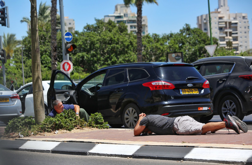 Israelis take cover as a siren sounds a warning of incoming rockets fired from the Gaza strip in the city of Ashkelon, southern Israel, on May 19, 2021. (credit: EDI ISRAEL/FLASH90)