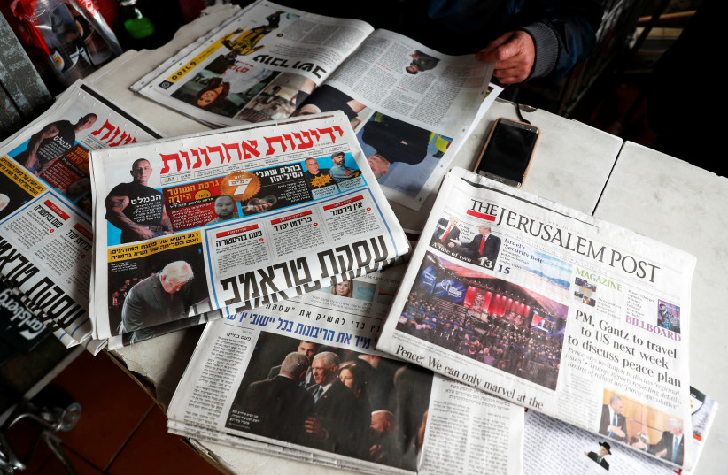 A man sits in a coffee shop next to the main Israeli Newspapers in Jerusalem (credit: RONEN ZVULUN/REUTERS)