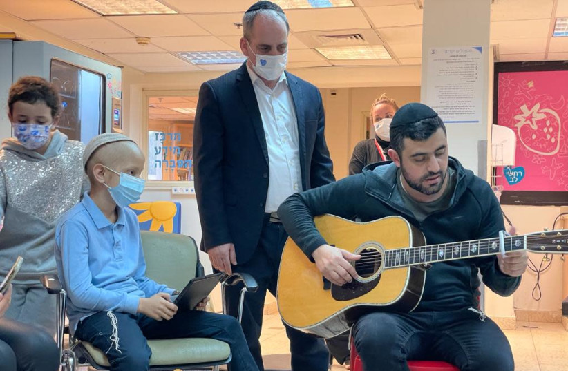 Ishay Ribo performing in the oncology department at Sheba Medical Center with Daniel, a 9-year-old cancer patient (credit: SHUKI BRIF)